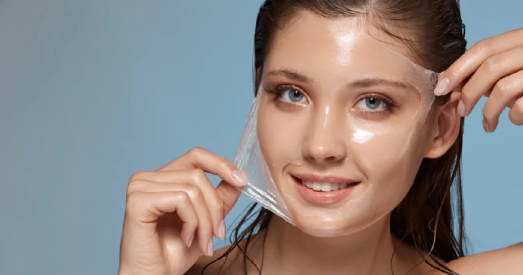 Young woman smiling while gently peeling off a clear, gel-like face mask, revealing glowing skin after Chemical Peels in Long Beach, CA.